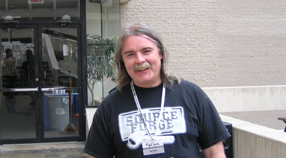 A photo of Tim Peters with long gray hair and a gray mustache wearing a Source Forge t-shirt